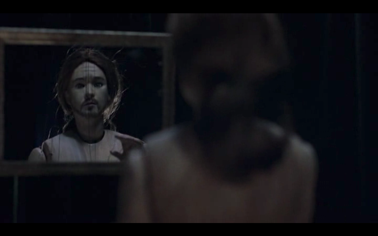 Still from the film "Being John Malkovich" in which a marionette puppet regards itself in a mirror